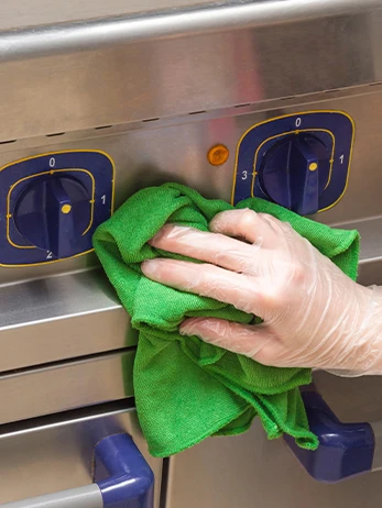 Wiping down catering equipment with a green cloth and safety PPE.
